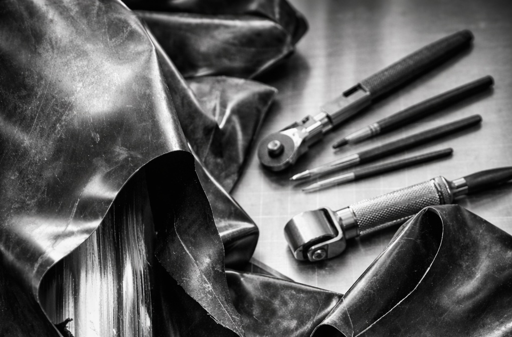 Detailaufnahme einer professionellen Latex Reparatur: beschädigtes schwarzes Latex auf einer Werkbank mit Reparaturwerkzeugen und sorgfältig ausgeführter Naht.